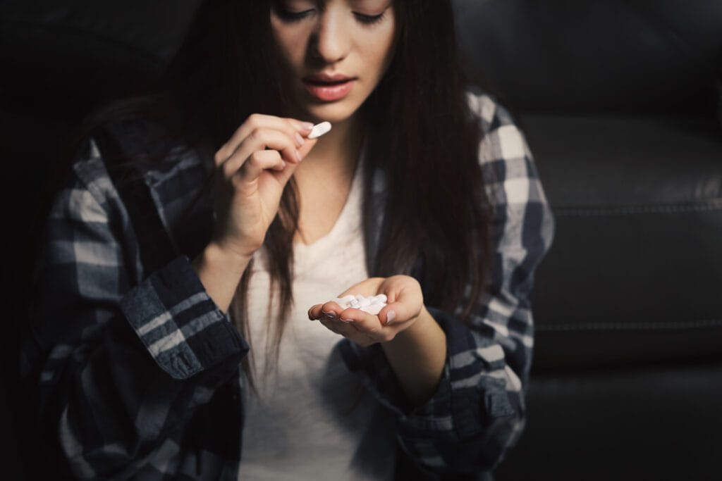 Young woman sitting near armchair and using pills