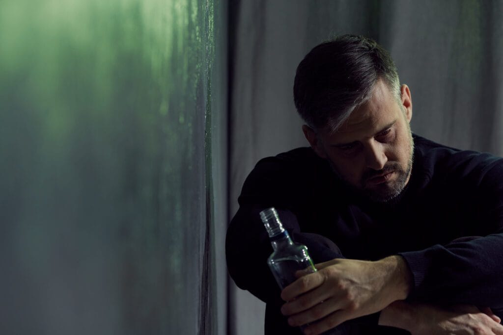 Alcohol addicted man sitting alone with alcohol bottle