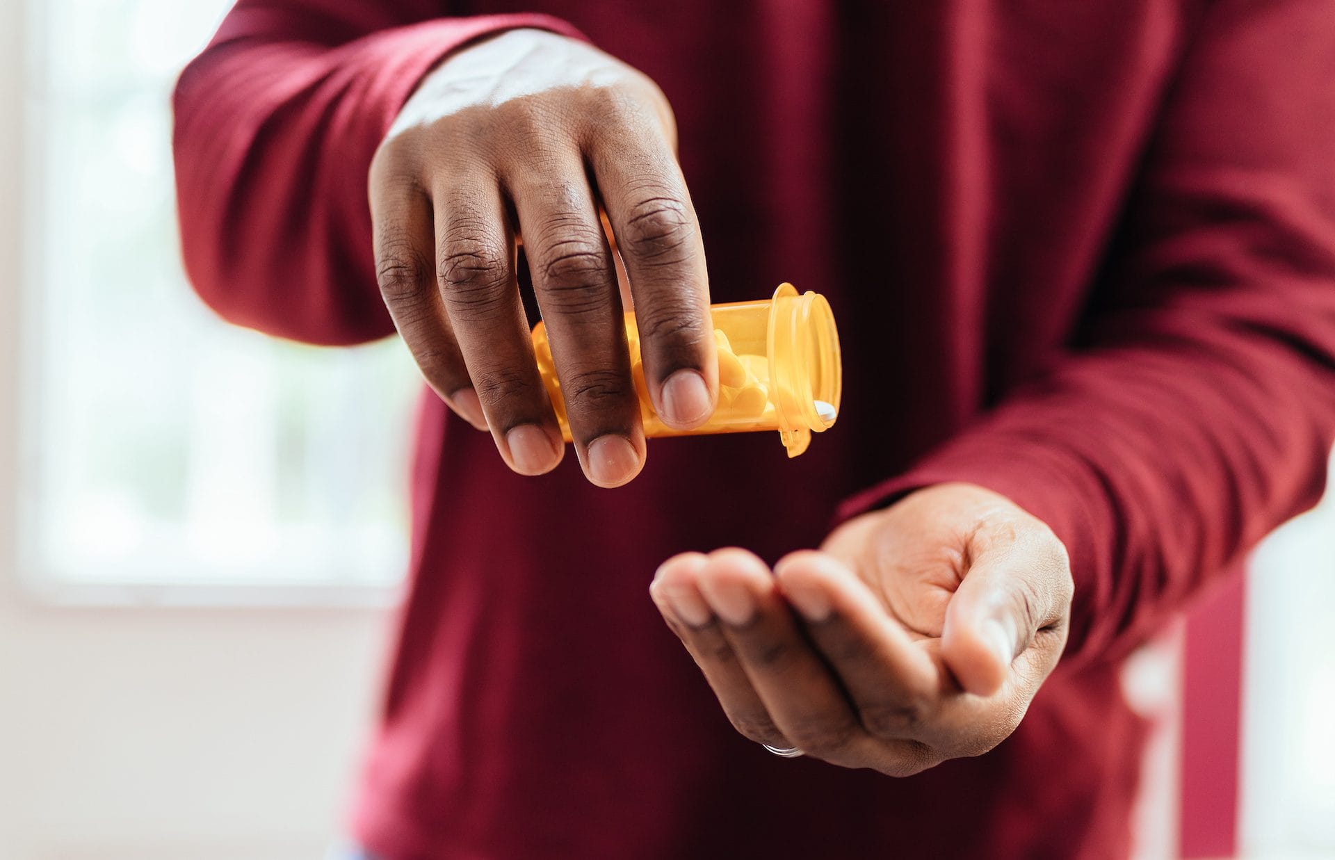 Man in red shirt pouring pills from prescription pill bottle