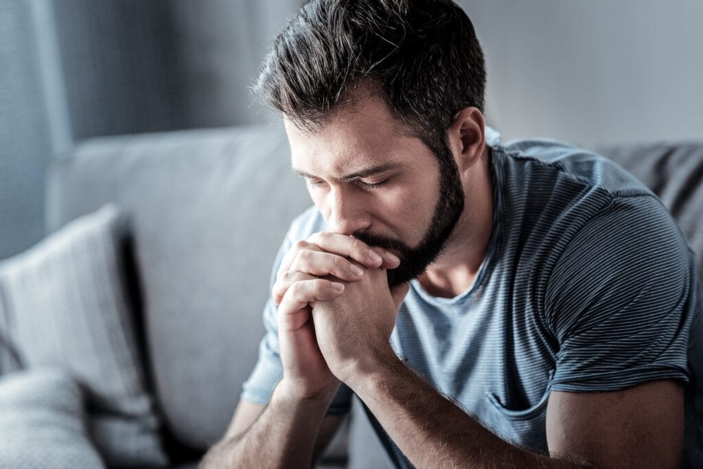 Unhappy man holding his chin and looking down while thinking what to do about his problem