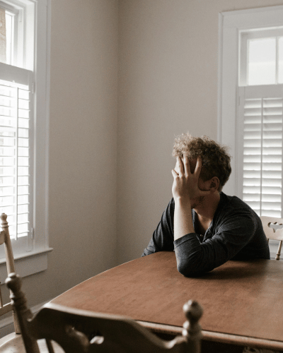 man looking out window with hand on head