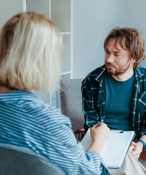 man in plaid shirt at therapy with a therapist who has a notebook open
